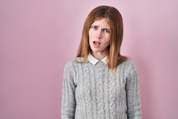 Fototapeta premium Beautiful woman standing over pink background in shock face, looking skeptical and sarcastic, surprised with open mouth