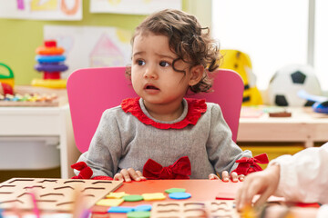 Adorable hispanic toddler playing with maths puzzle game sitting on table at kindergarten