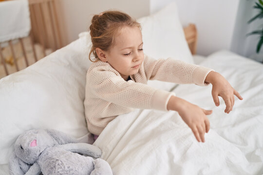 Adorable blonde girl somnambulist sitting on bed at bedroom
