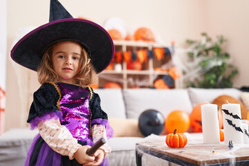 Adorable hispanic girl wearing halloween witch costume holding broom at kindergarten