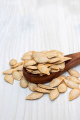 Pumpkin Seeds in a Wooden Spoon Isolated on White Wooden Background