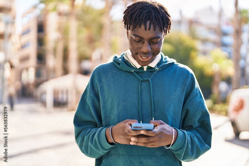 Wall mural African american man smiling confident using smartphone at street