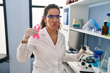 Young hispanic woman working at scientist laboratory looking for breast cancer cure depressed and worry for distress, crying angry and afraid. sad expression.