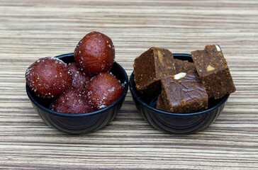 Closeup of Kala Jamun and Other Indian Sweets in a Black Bowls Isolate on Wooden Background