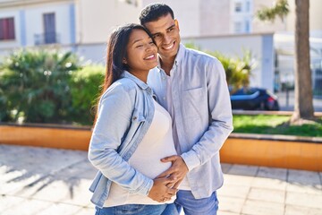 Young latin couple expecting baby hugging each other standing at park