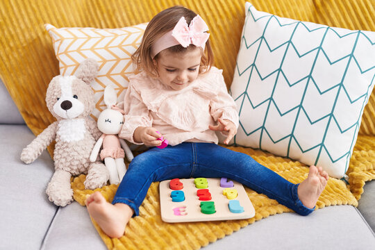 Adorable blonde toddler playing with maths puzzle game sitting on sofa at home