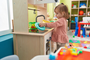 Adorable blonde girl playing with play kitchen standing at kindergarten