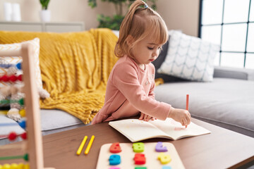 Adorable blonde girl drawing on notebook at home