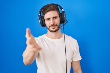 Hispanic man with beard listening to music wearing headphones smiling cheerful offering palm hand giving assistance and acceptance.