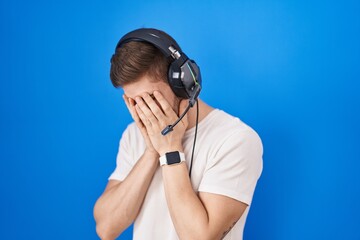 Hispanic man with beard listening to music wearing headphones with sad expression covering face with hands while crying. depression concept.