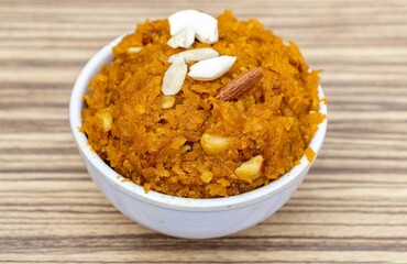 Closeup of Homemade Gajar Ka Halva or Carrot Halwa Garnished with Cashew and Almond Nut Cuts Isolate on Wooden Background