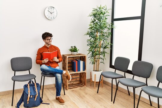 Young hispanic man smiling confident reading book at waiting room