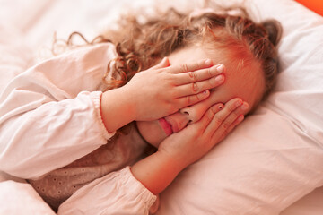 Fototapeta na wymiar Adorable blonde toddler stressed lying on bed covering eyes with hands at bedroom