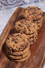 Homemade chocolate chip cookies stacked on a wooden chopping board. With a blue tile background