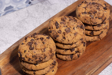 Homemade chocolate chip cookies stacked on a wooden chopping board. With a blue tile background
