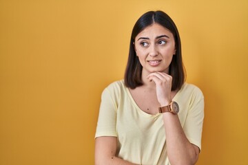 Hispanic girl wearing casual t shirt over yellow background thinking worried about a question, concerned and nervous with hand on chin