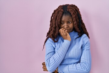 African woman standing over pink background looking stressed and nervous with hands on mouth biting nails. anxiety problem.