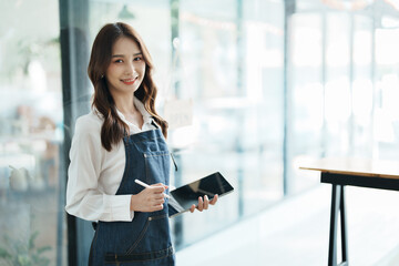 Fototapeta premium open a small business Portrait of happy Asian woman in apron holding tablet in front of cafe.