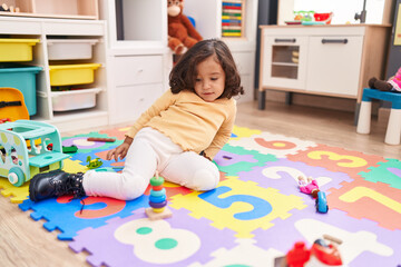 Adorable hispanic toddler playing with hoops toy sitting on floor at kindergarten