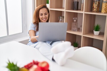 Fototapeta premium Young woman using laptop sitting on table at home