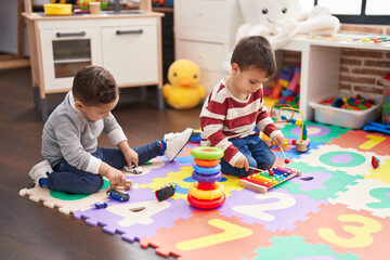 Fototapeta premium Two kids playing xylophone holding car toy sitting on floor at kindergarten
