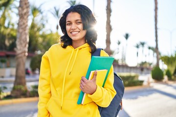 Young latin woman student smiling confident holding books at street