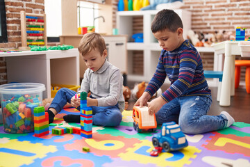 Two kids playing with construction blocks and truck toy sitting on floor at kindergarten