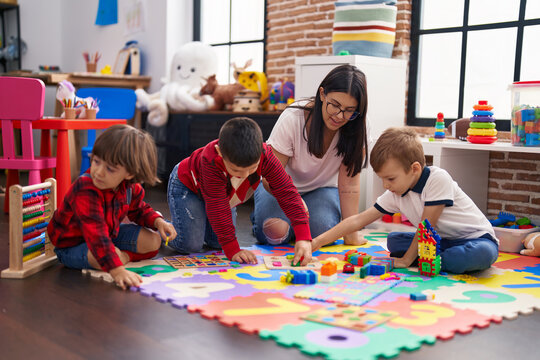 Teacher with group of boys playing with maths puzzle game sitting on floor at kindergarten