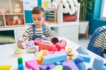 Adorable caucasian boy sitting on table playing with toys at kindergarten