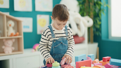 Adorable caucasian boy playing with construction blocks at kindergarten