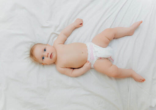 a happy joyful baby in diapers is lying on a white bed and holding his leg. High-quality photo. place for text