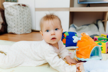 A six-month-old baby plays on the floor with colorful toys. The baby learns to crawl. portrait of a 6 month old baby