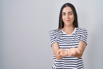 Obraz premium Young brunette woman wearing striped t shirt smiling with hands palms together receiving or giving gesture. hold and protection