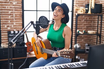 Fototapeta na wymiar Young hispanic woman musician singing song playing classical guitar at music studio
