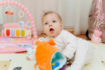 a cute little baby of 6 months is sitting on a carpet among colorful toys. a child is playing with a toy