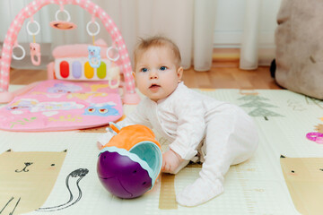 a cute little baby of 6 months is sitting on a carpet among colorful toys. a child is playing with a toy