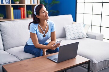 Obraz premium Young beautiful hispanic woman using smartphone and laptop at home