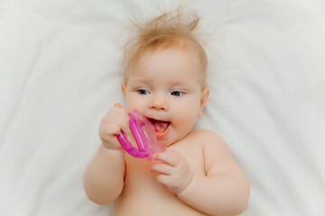 The child grows the first tooth. Smiling baby 6 months old chewing teether in bed closeup