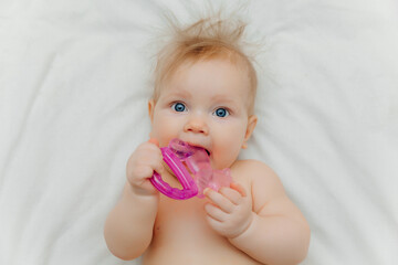 The child grows the first tooth. Smiling baby 6 months old chewing teether in bed closeup