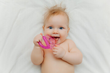 The child grows the first tooth. Smiling baby 6 months old chewing teether in bed closeup