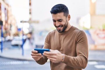 Young hispanic man smiling confident using smartphone at street