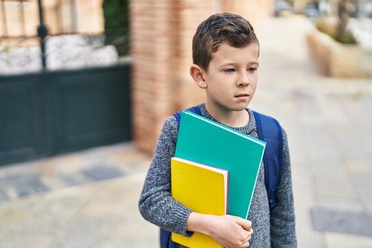 Blond child student holding books standing at street