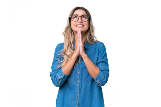 Young Uruguayan woman over isolated background keeps palm together. Person asks for something