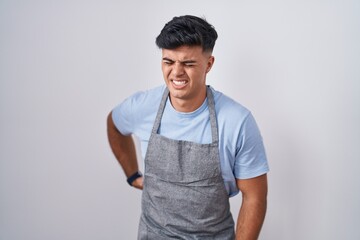 Hispanic young man wearing apron over white background suffering of backache, touching back with hand, muscular pain