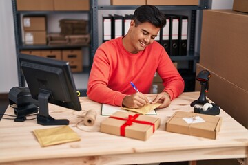 Young hispanic man ecommerce business worker writing on package at office