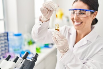 Young beautiful hispanic woman scientist holding liquid at laboratory