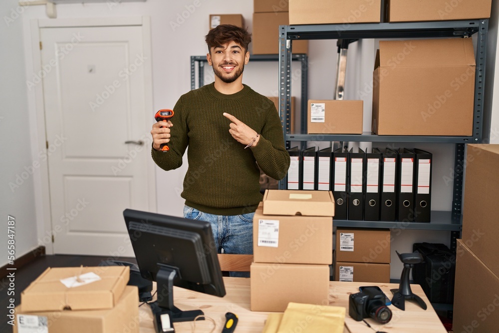 Sticker Arab man with beard working at small business commerce holding bar code scanner smiling happy pointing with hand and finger