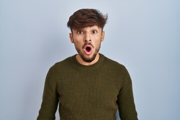 Arab man with beard standing over blue background afraid and shocked with surprise expression, fear and excited face.