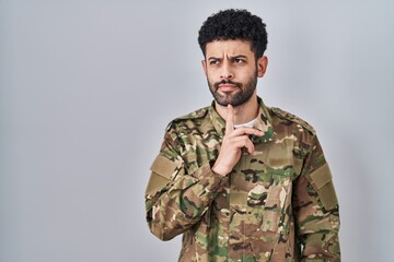 Arab man wearing camouflage army uniform thinking concentrated about doubt with finger on chin and...