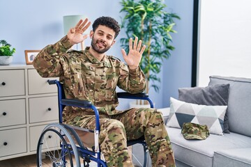 Fototapeta premium Arab man wearing camouflage army uniform sitting on wheelchair showing and pointing up with fingers number nine while smiling confident and happy.